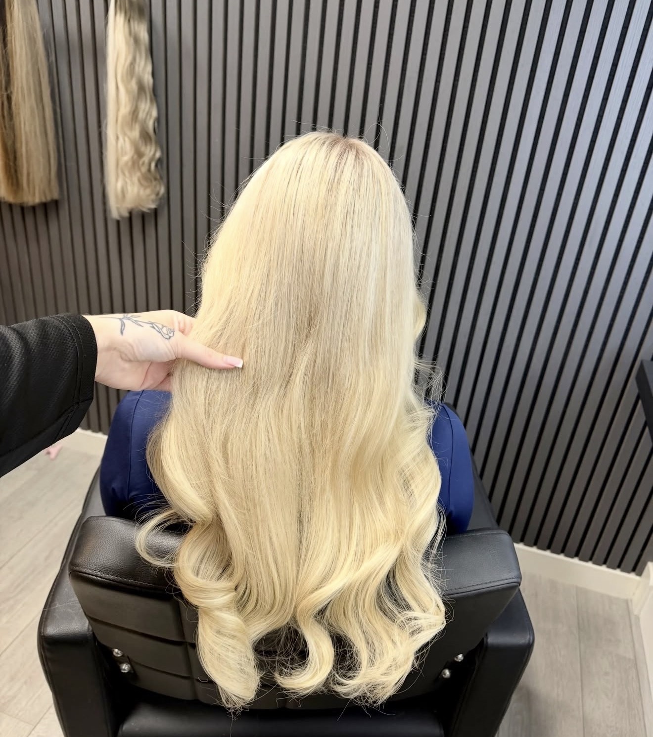 Lang, heel licht blond haar met golven in de stoel bij May Blonde, met extensions aan het rek op de achtergrond