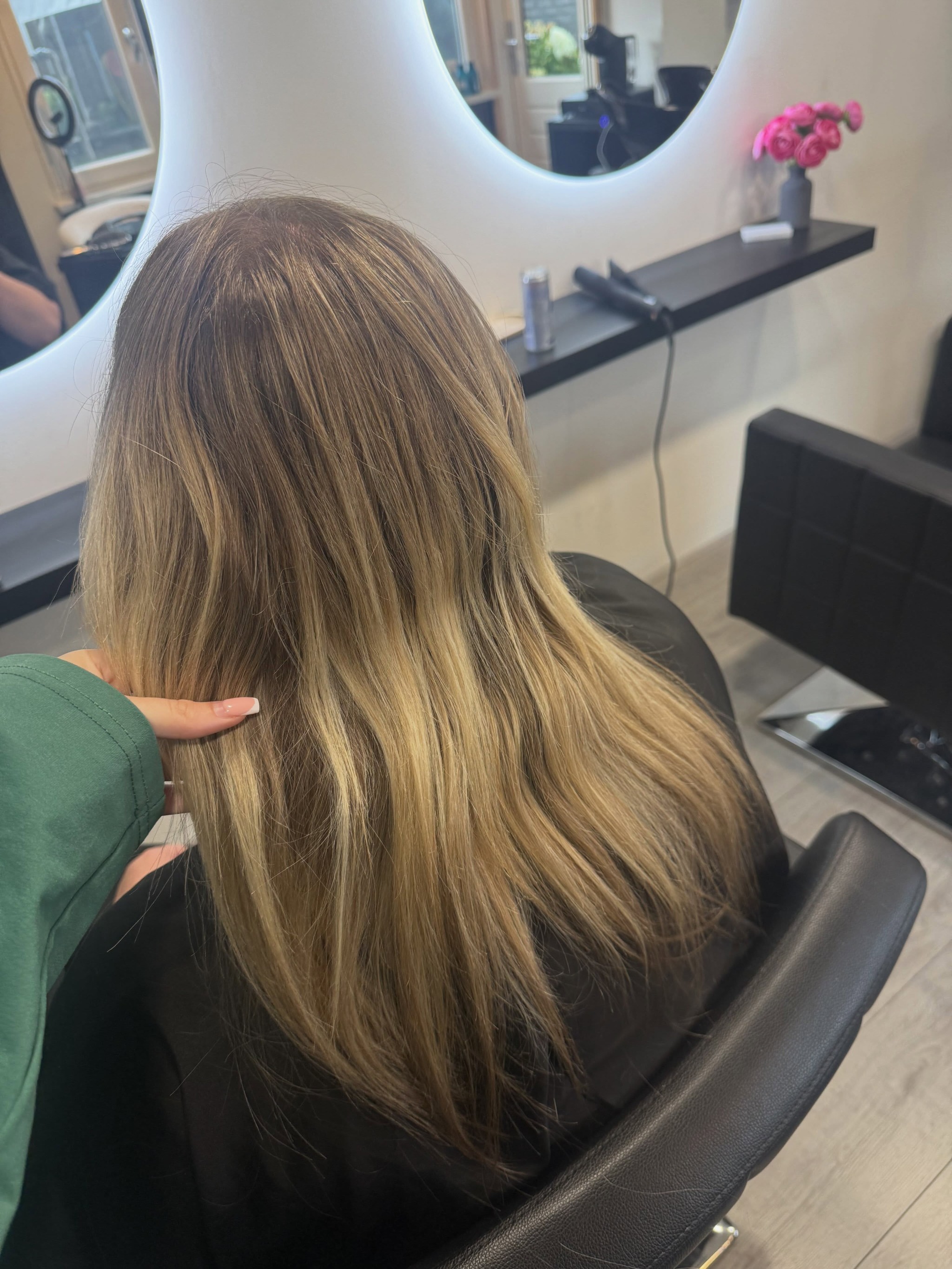 Lang bruinblond haar in de stoel, met de ronde verlichte spiegel op de achtergrond